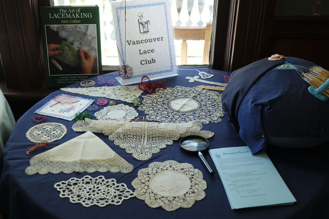 Cream-coloured lace doilies and various shapes placed on a dark blue tablecloth with sign that says Vancouver Lace Club