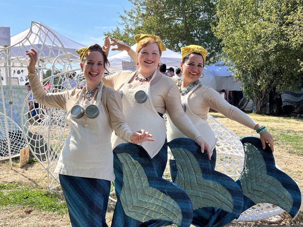 Three women dressed as mermaids with headkerchiefs, aprons, and cans.