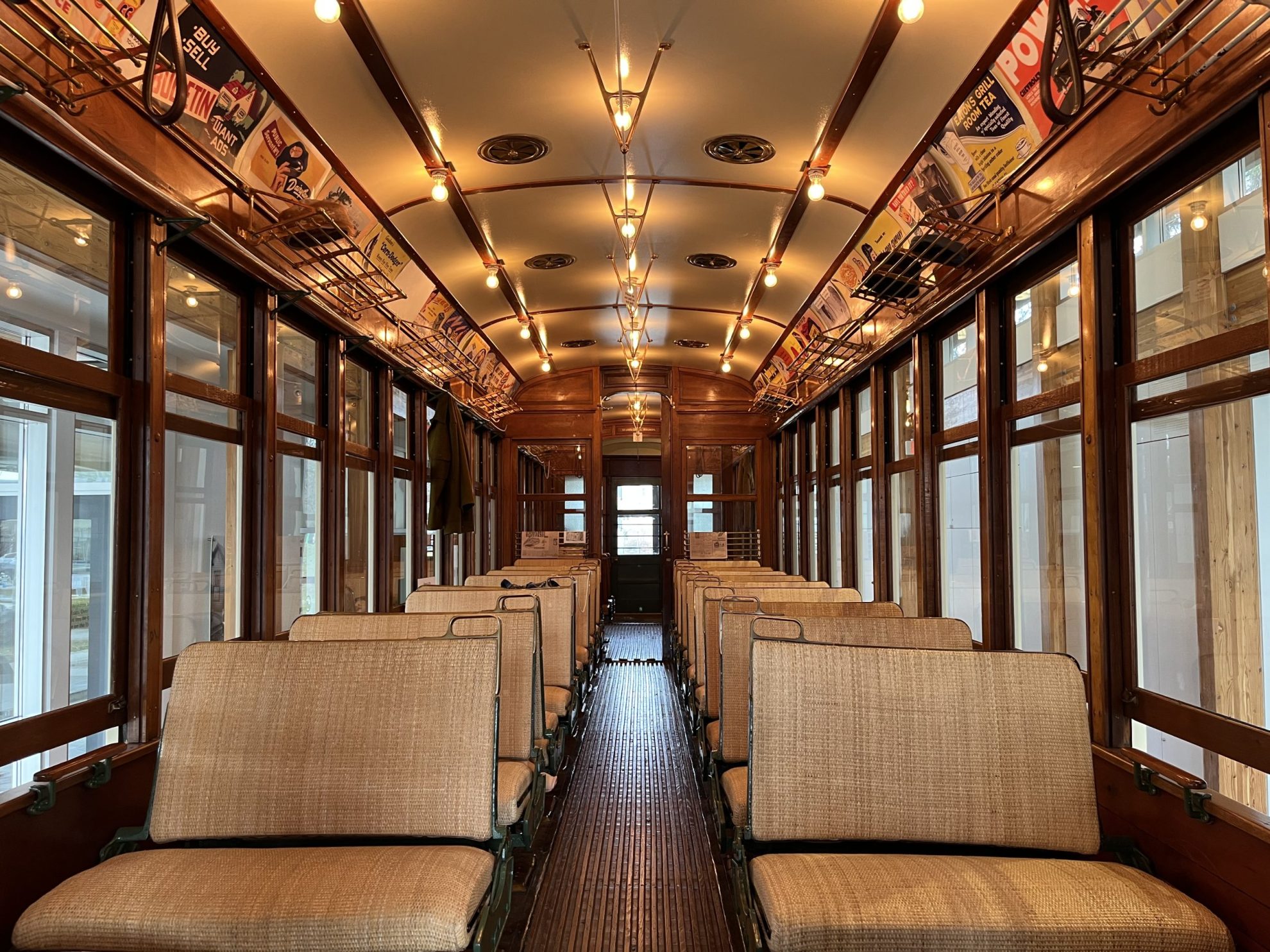 Interior of a wooden tram car lined two rows of wicker chairs and vintage advertising posters hung on the sides.