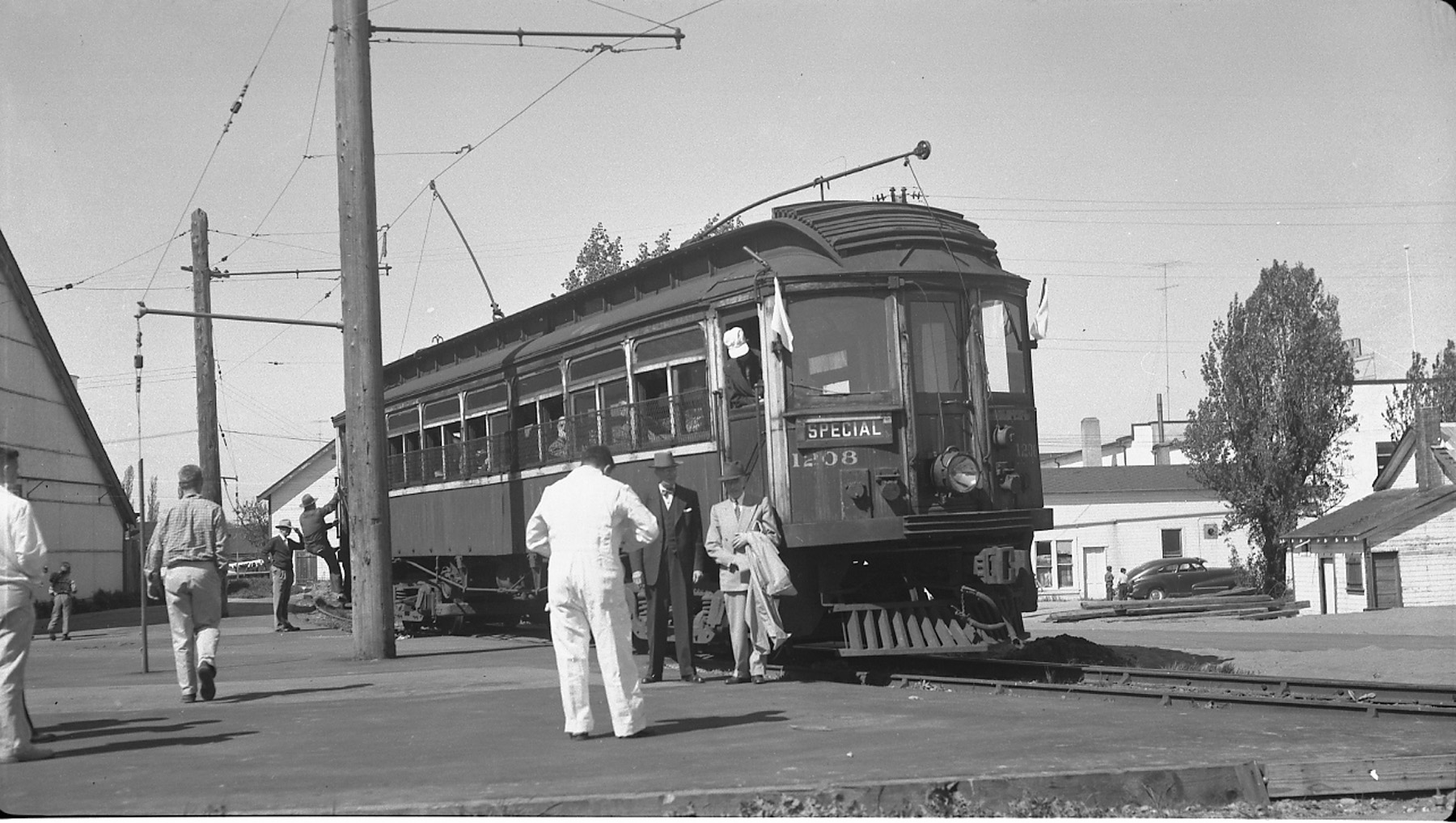Black and white photo of tram car with two men standing in forefront.