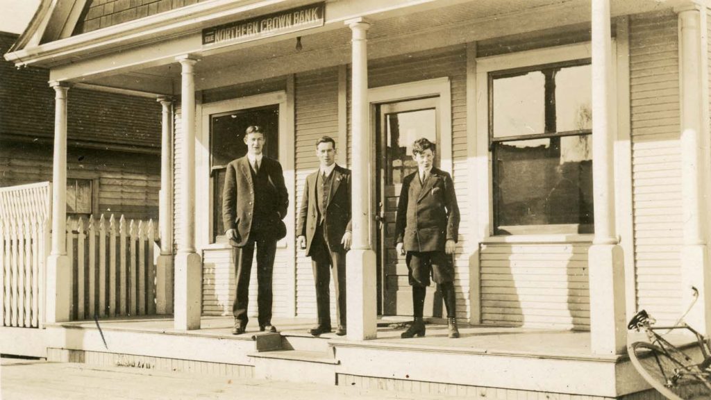 Black and white photo of four men in suits standing in front of an old bank building. 