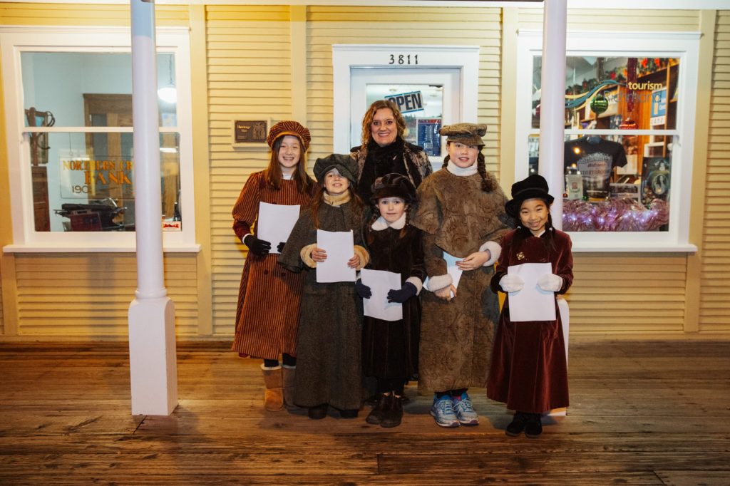 Six people standing in old-fashioned outfits holding music sheets