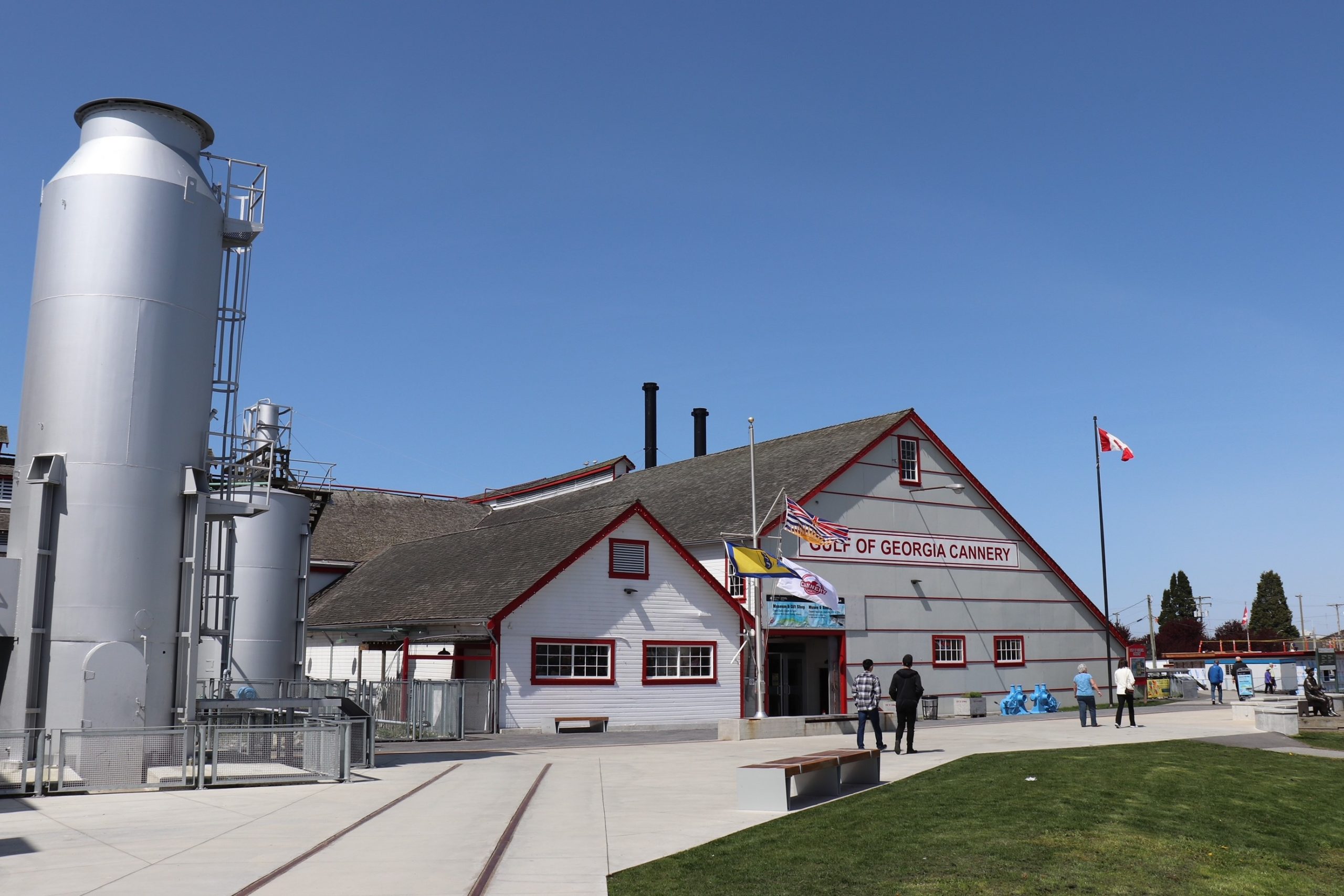 Exterior view of the Gulf of Georgia Cannery National Historic site, a white building with red trim, metallic tanks to the left and a Canada flag to the right