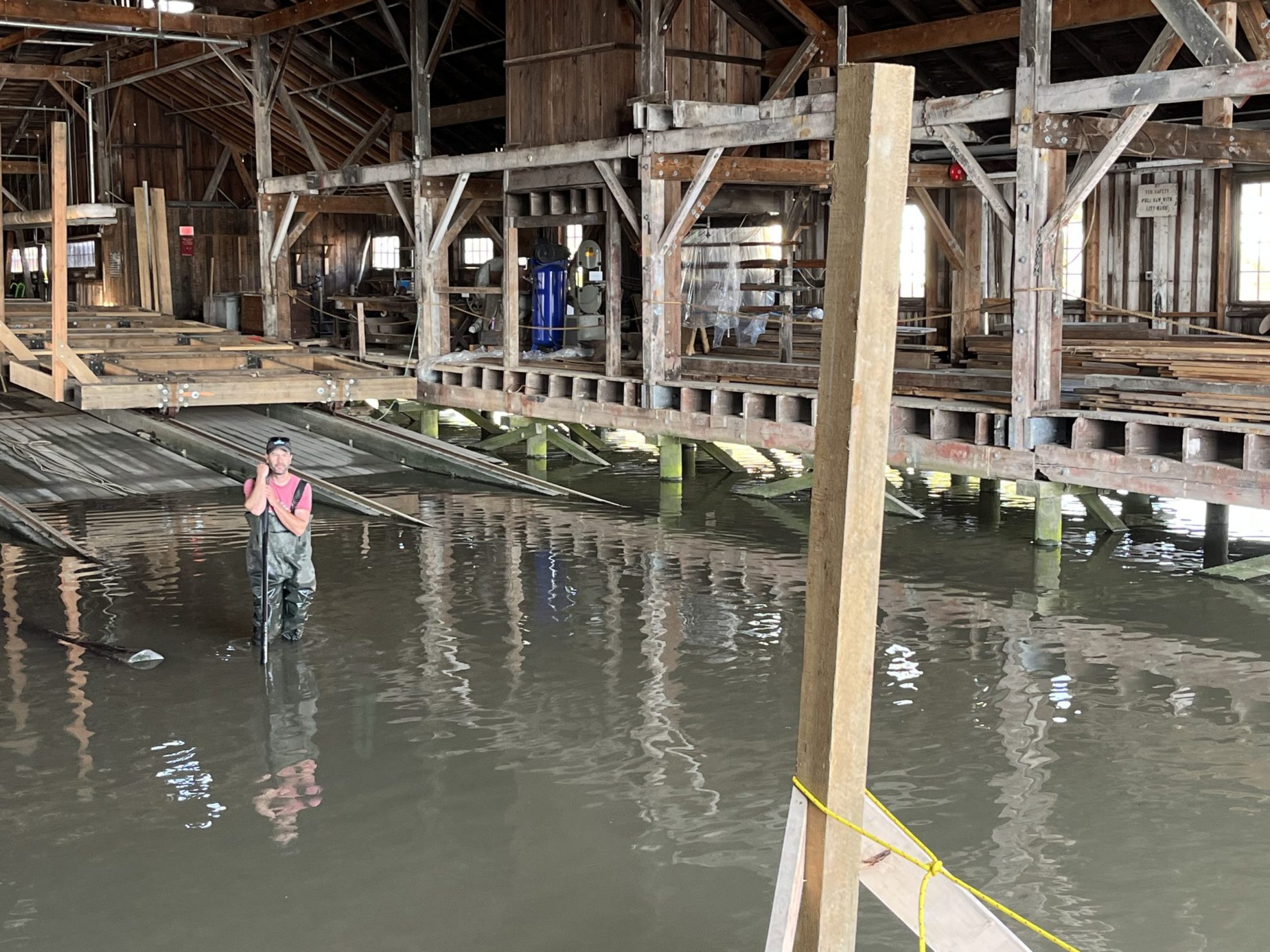 Man in red shirt and hipwaders in water inside historic wooden building