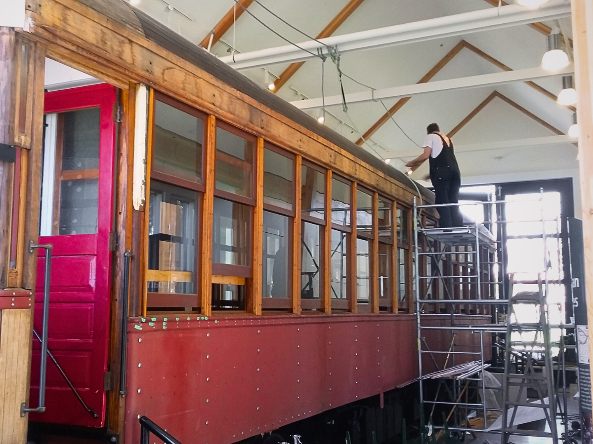 Side view of Tram Car 1220 mid-restoration with carpenter tending to its roof.
