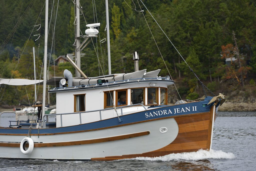 The Sandra Jean II (boat with a white, blue, and wooden textured hull) sailing on the water.