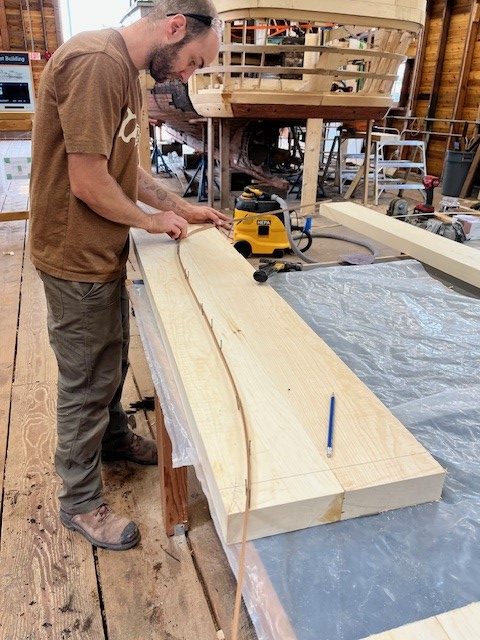 Man in brown shirt measuring a curved shape on a thick flat piece of wood