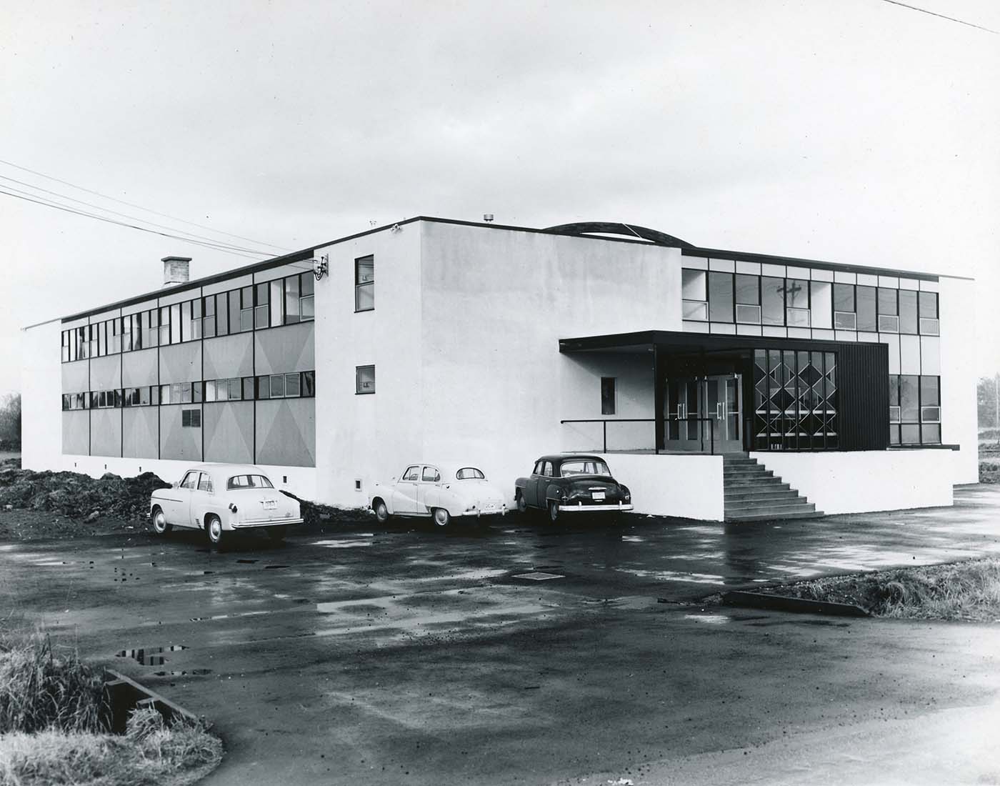 black and white photo of two-storey building with cars parked in front