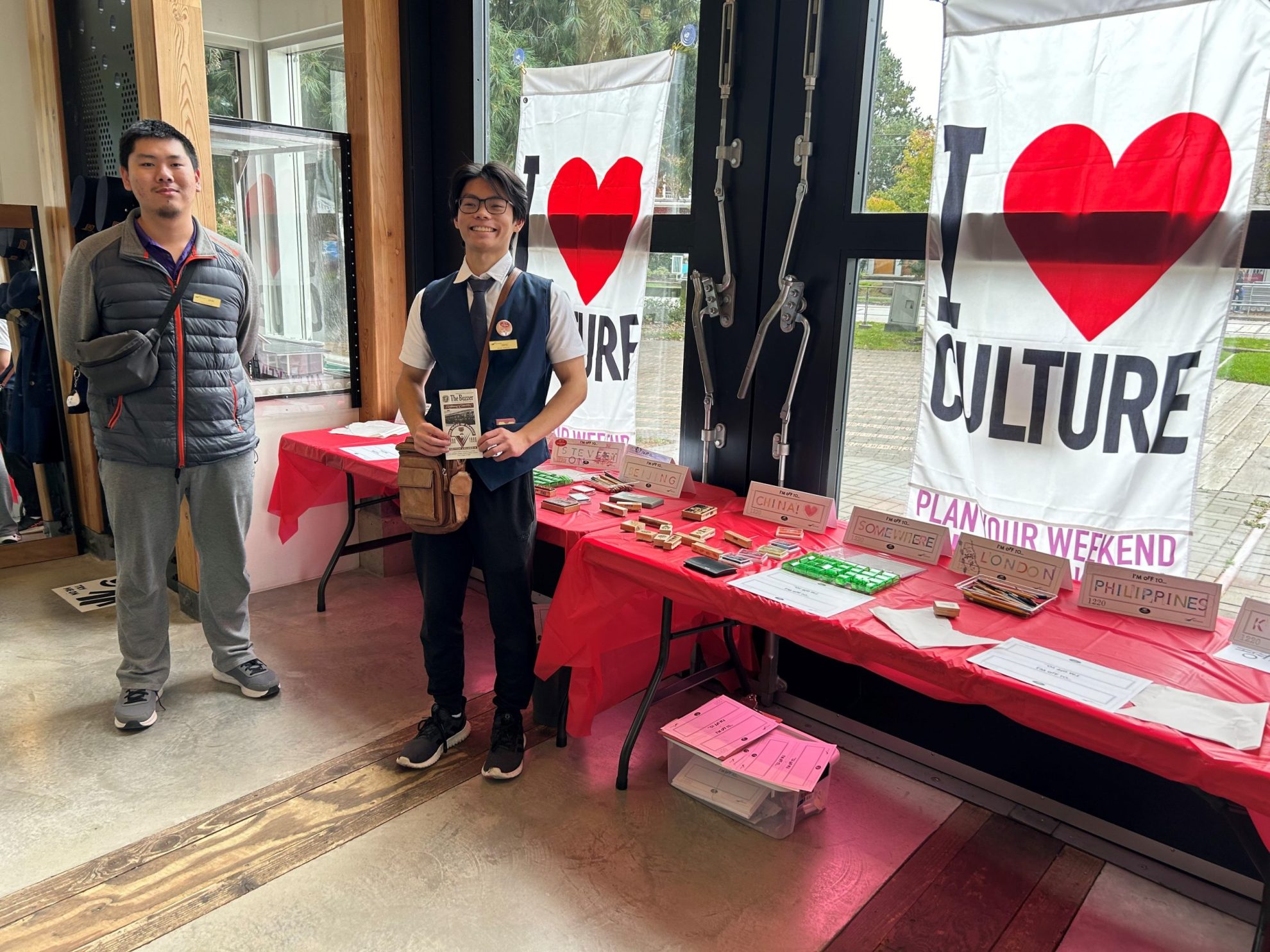 Two men standing in front of "I (heart) culture" banners and a table with red tablecloth