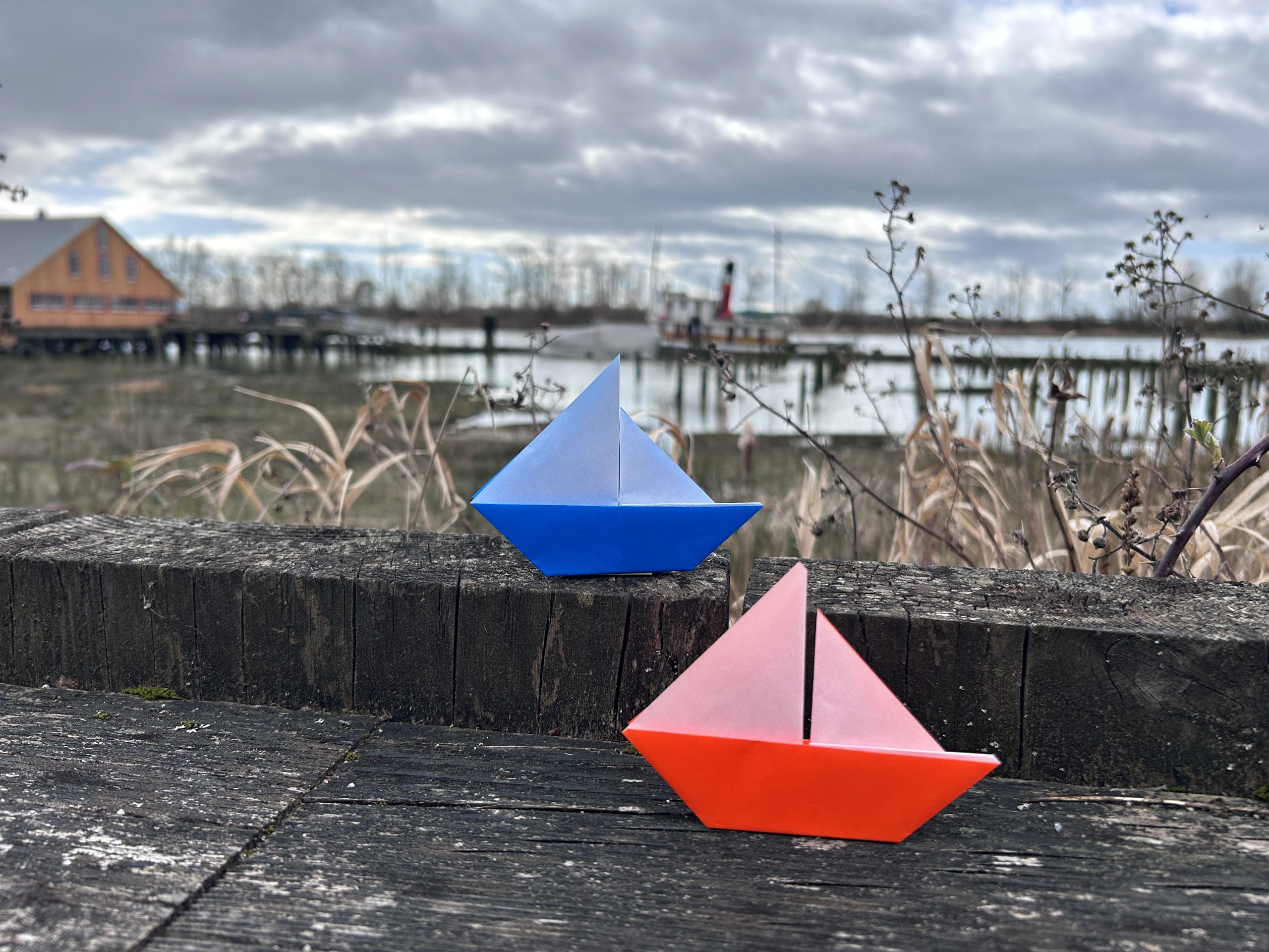 a red and a blue sailboat made of origami displayed in front of tidal marsh