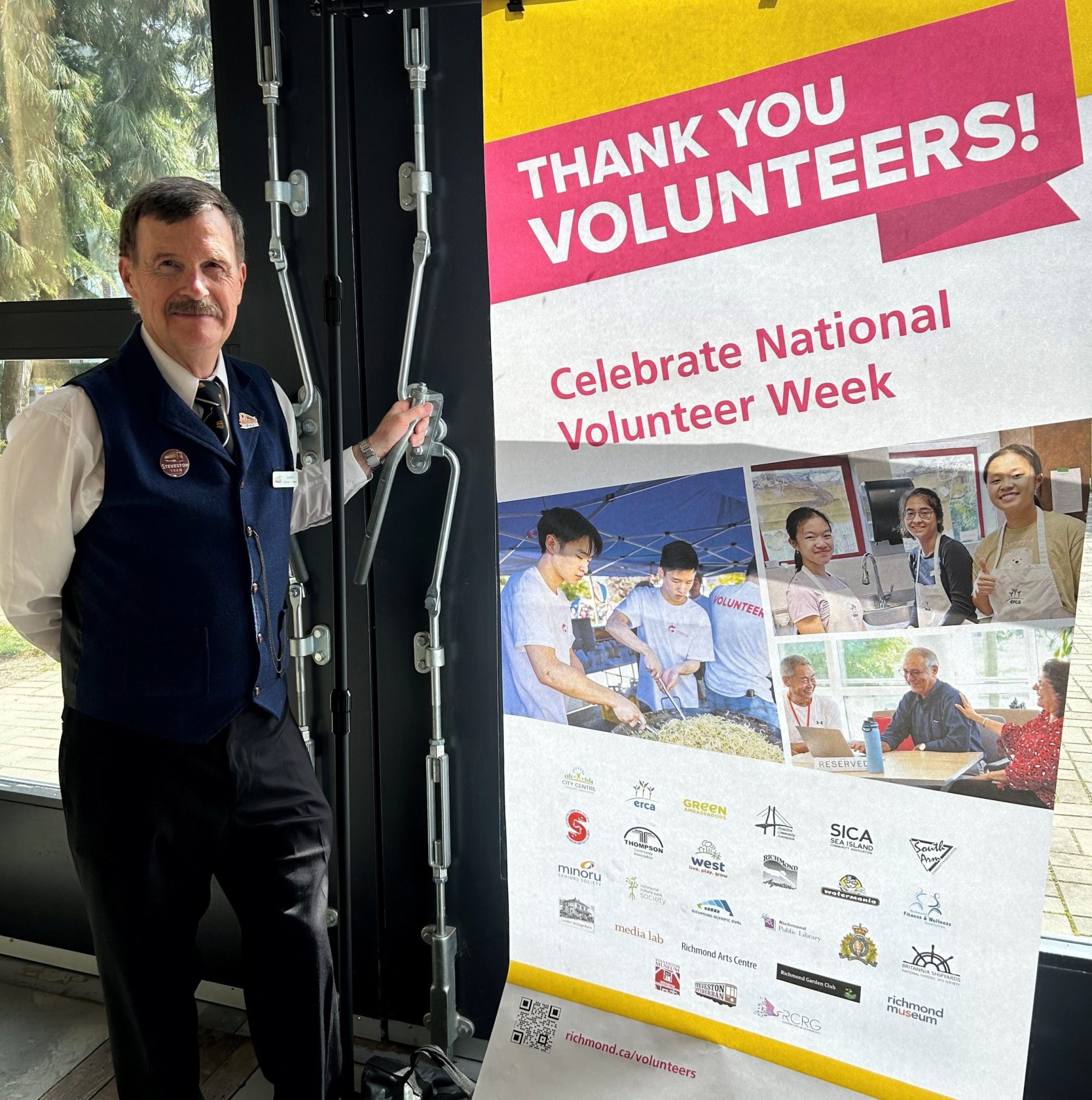 Man in conductor uniform standing beside a Volunteer Week poster