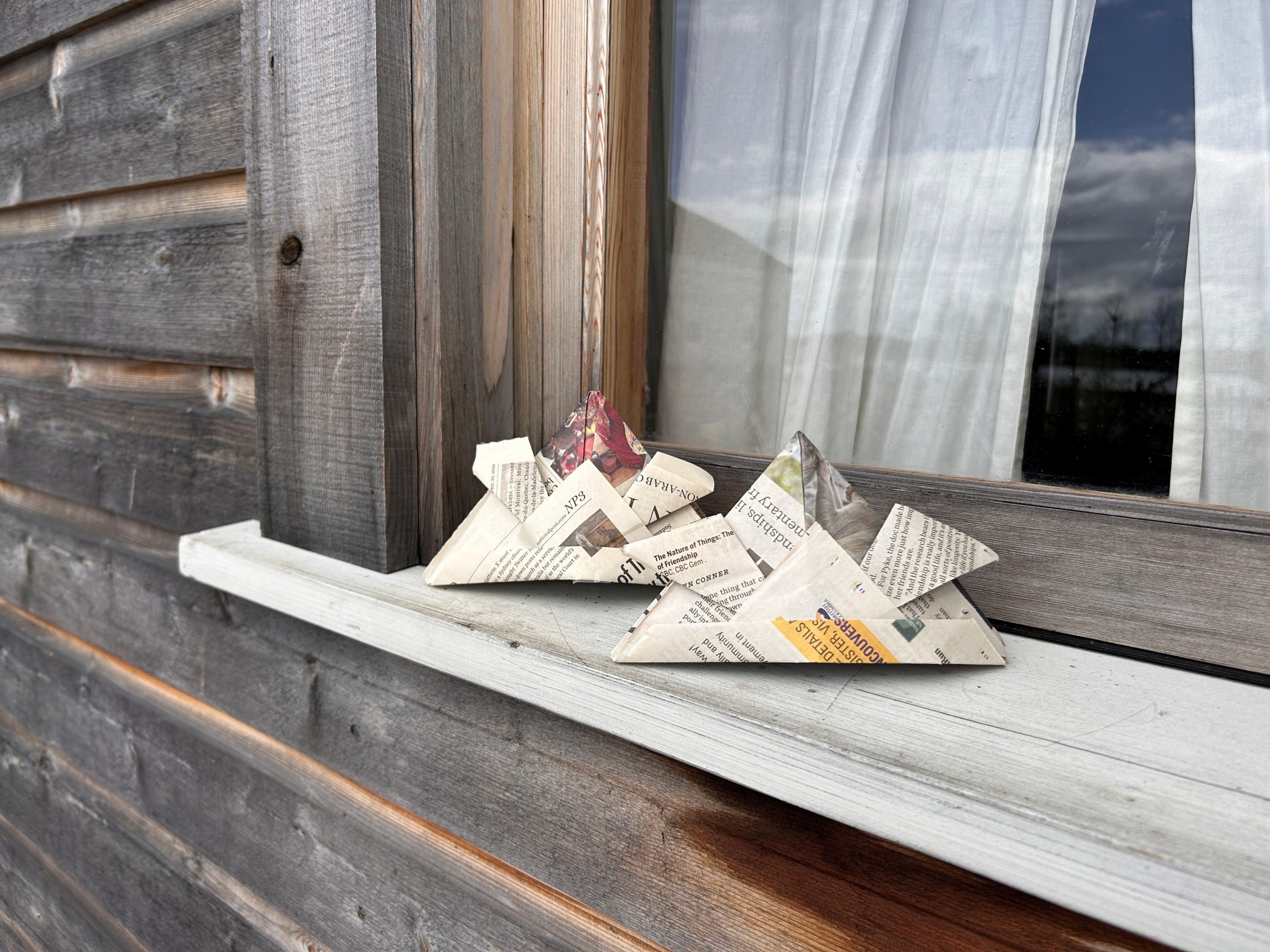 Small origami samurai hats made of folded newspaper displayed on a window sill