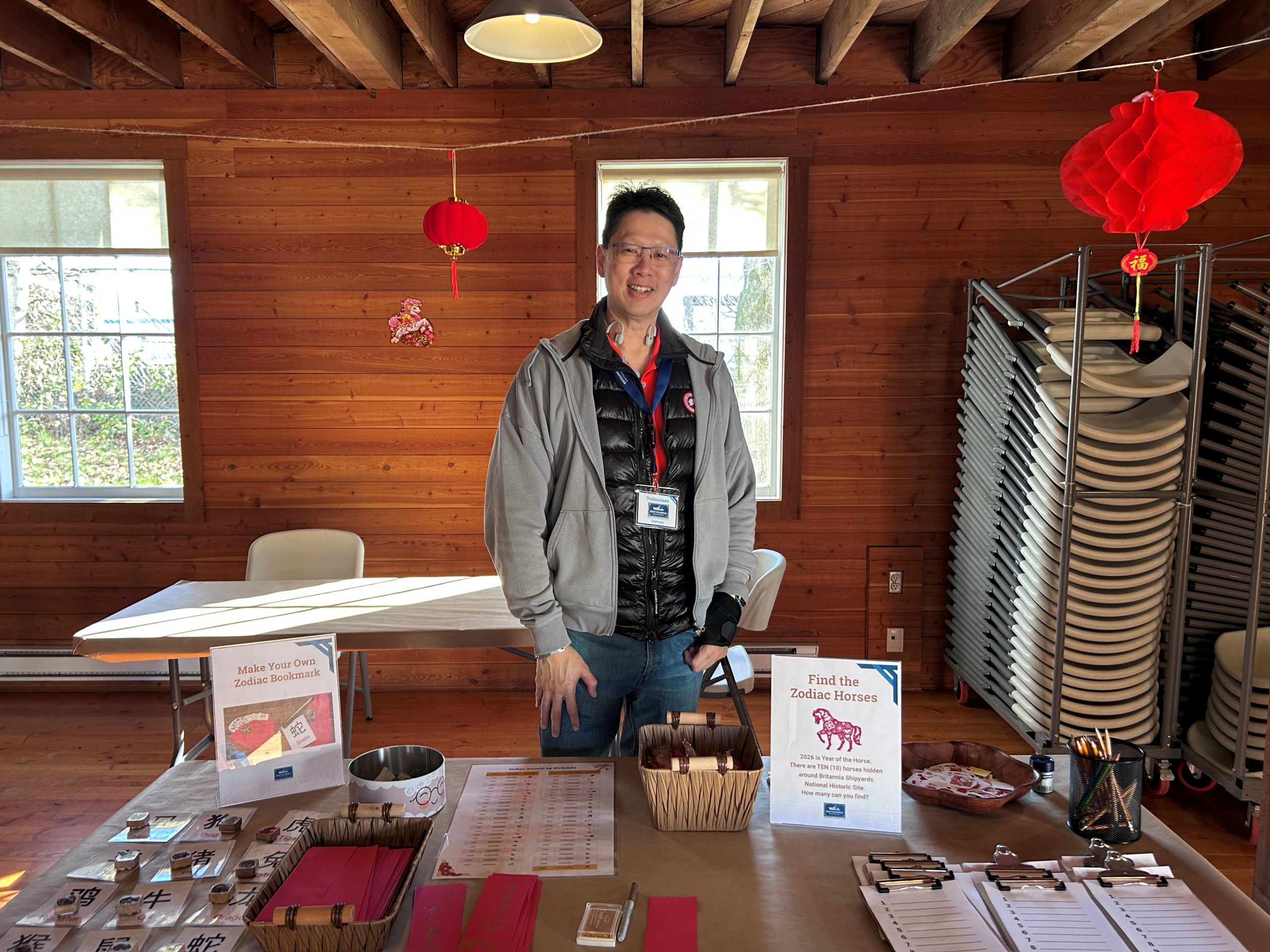 man with glasses wearing grey jacket and standing behind a lunar new year activity table