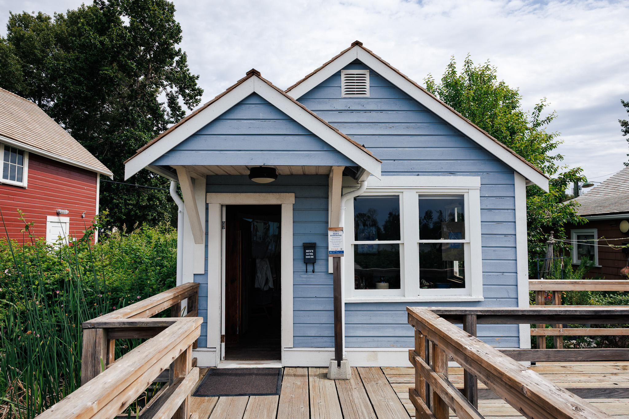 Light blue stilt house with open doorway and white framed window.