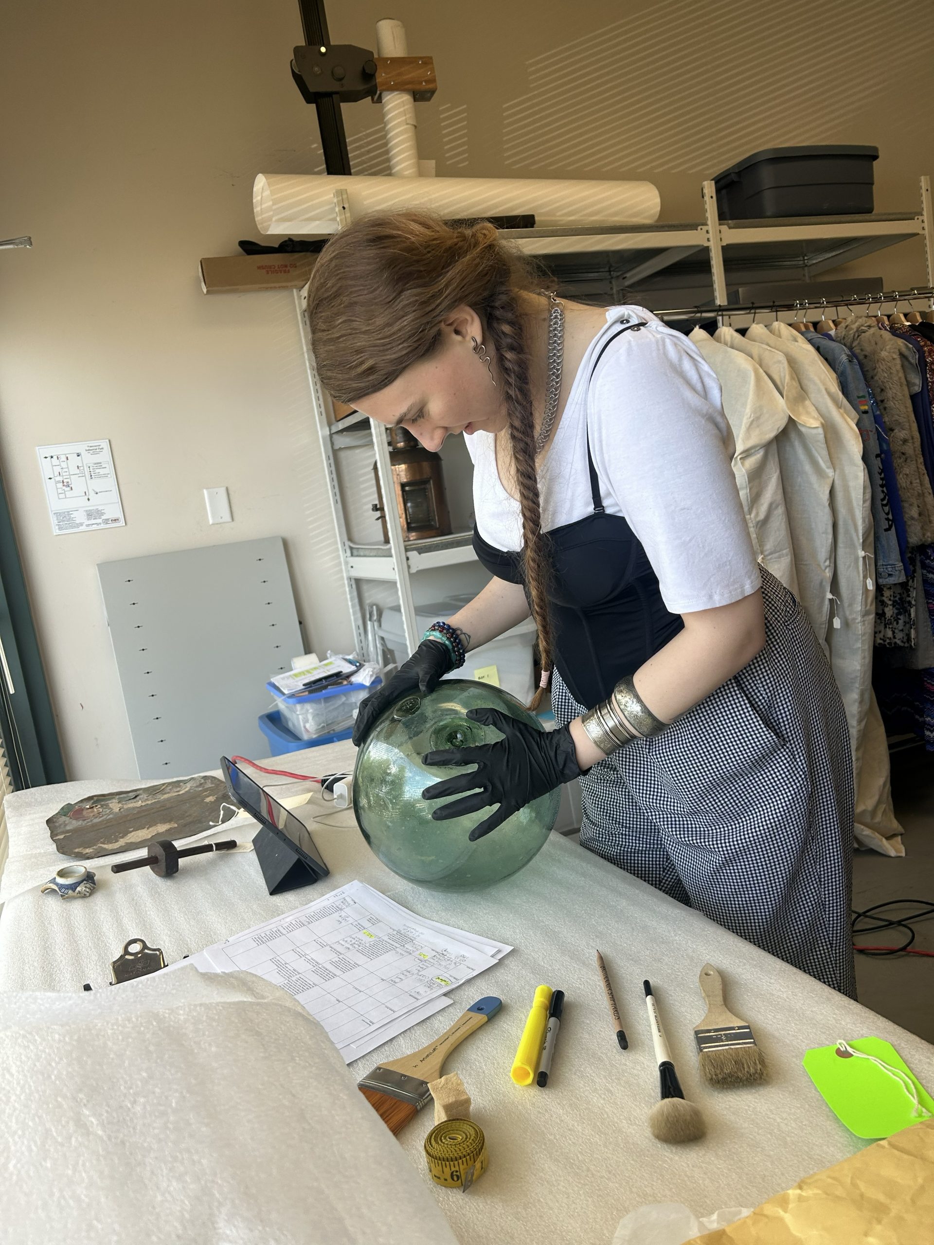 Woman with braids wearing white shirt and apron cleaning a large Japanese glass float
