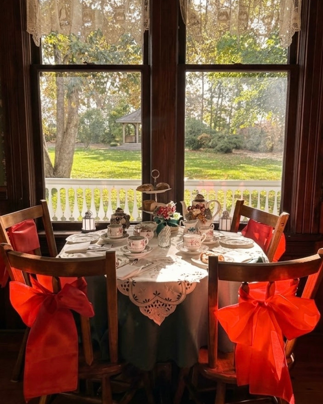 Afternoon tea served on table with white tablecloth and chairs decorated with big red bows